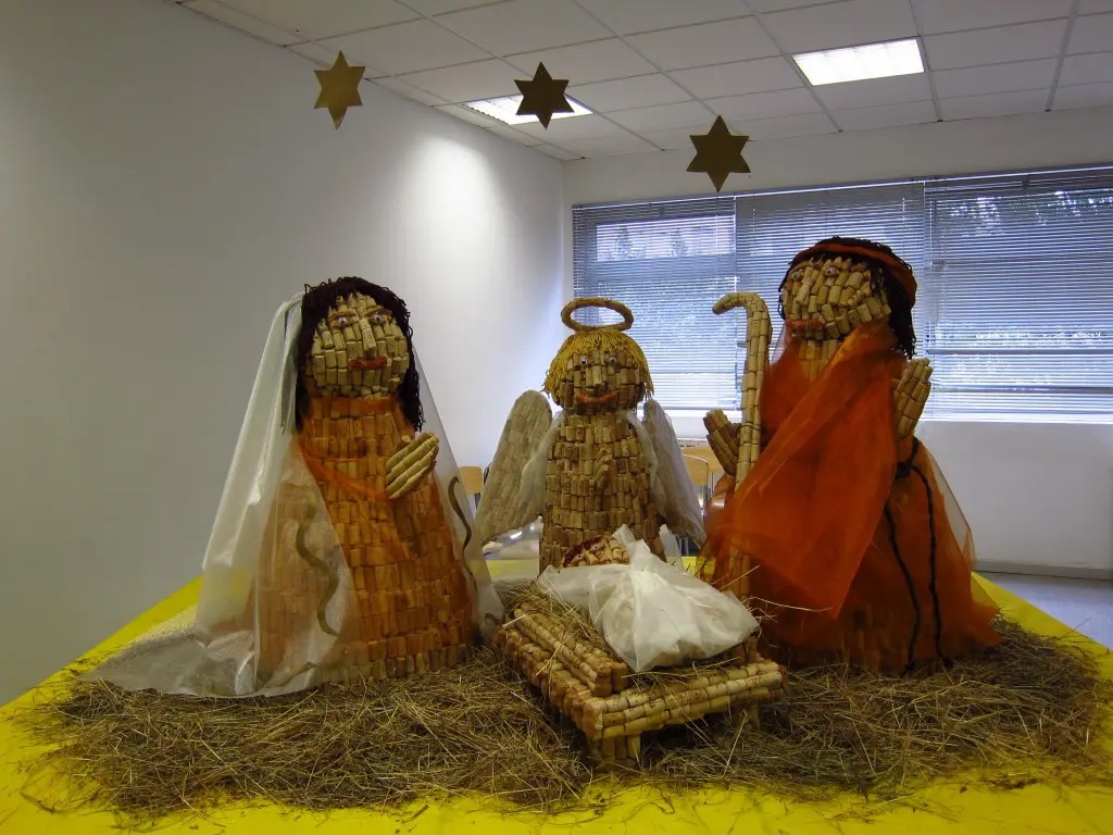 Presépio com figuras feitas de rolhas de cortiça, sobre palha, com estrelas penduradas por cima