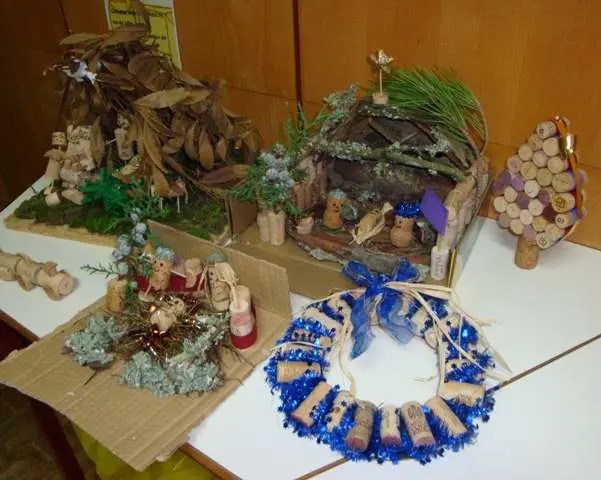 Trabalhos de Natal feitos com rolhas: presépios, uma grinalda azul e uma árvore, sobre uma mesa